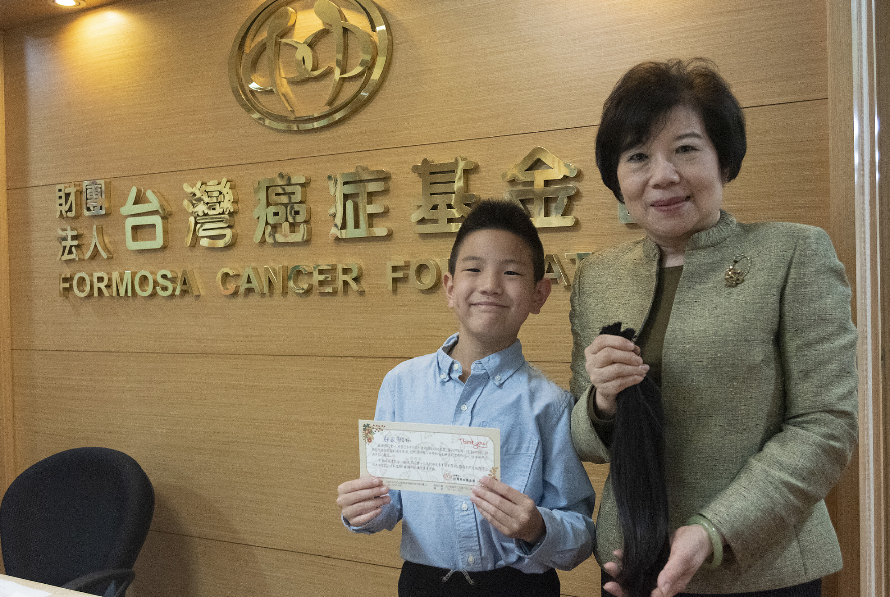 台灣癌症基金會蔡麗娟副執行長(圖右)接受敏睿(圖左)捐髮並頒贈感謝小卡。